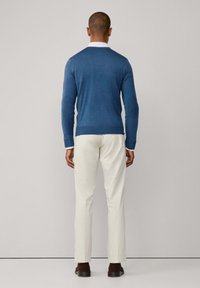Maglione blu lavorato a maglia con collo rotondo, abbinato a pantaloni color crema. L'outfit presenta una linea dritta e una texture liscia.