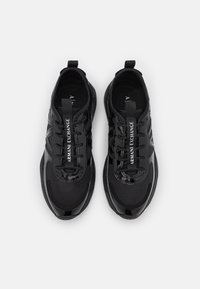 Scarpe da ginnastica nere realizzate con una combinazione di materiali lisci e testurizzati, dotate di lacci e con la scritta "ARMANI EXCHANGE" stampata sulla linguetta.