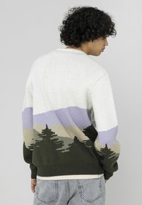 Pull en tricot avec un motif pittoresque comprenant des arbres et des montagnes. Couleurs : crème, vert, lavande et taupe. Ourlet et poignets côtelés.