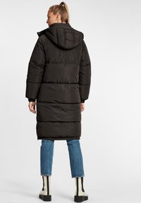 Svart puffjacka med huva, med ett söm mönster, elastiska ärmslut och sidofickor, tillsammans med blå jeans och randiga stövlar.