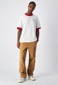 Biała koszulka z krótkim rękawem z czerwonym kołnierzykiem i mankietami, w połączeniu z beżowymi spodniami i białymi trampkami z czarnymi akcentami. Swobodny fason, minimalistyczny design.