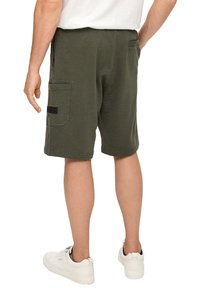 Olivgrüne Baumwollshorts mit einer lockeren Passform, ausgestattet mit seitlichen Taschen und einer aufgesetzten Gesäßtasche. Tragen Sie dazu weiße Sneakers.