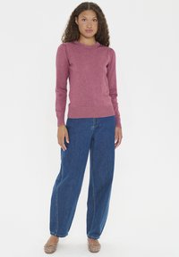 Suéter de punto burdeos con mangas largas, puños y dobladillo acanalados; combinado con vaqueros de mezclilla azul de talle alto y bailarinas beige adornadas.