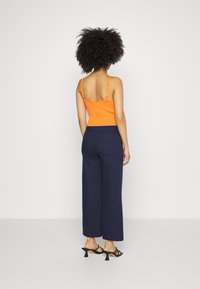 Oranžový ribbed top s vlnitými okraji, spárovaný s vysokým pasem námořnickými širšími kalhotami a černými sandály na podpatku.