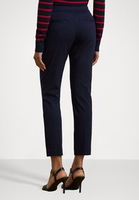 Navy tailored trousers with a fitted silhouette, back pockets, and a smooth fabric finish, complemented by sleek black high-heeled sandals.