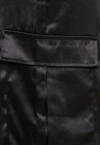 Mustat satiini kangas, jossa on sileä pinta, litteä taskusuunnittelu ja hienovarainen kiilto, jota korostavat siististi ommellut reunat.