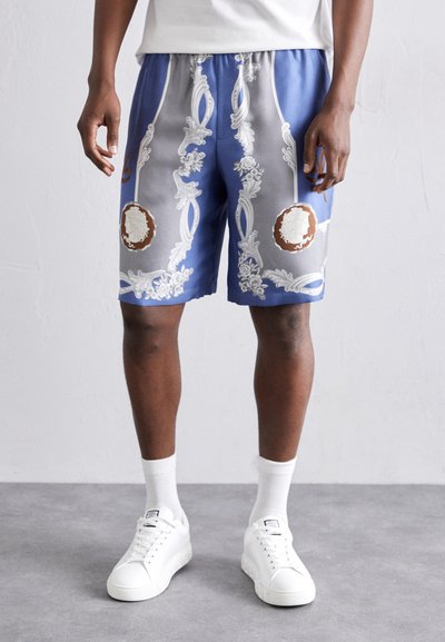 Blue shorts with ornate white floral patterns and brown accents. Elastic waistband with drawstring, smooth fabric, knee-length design.