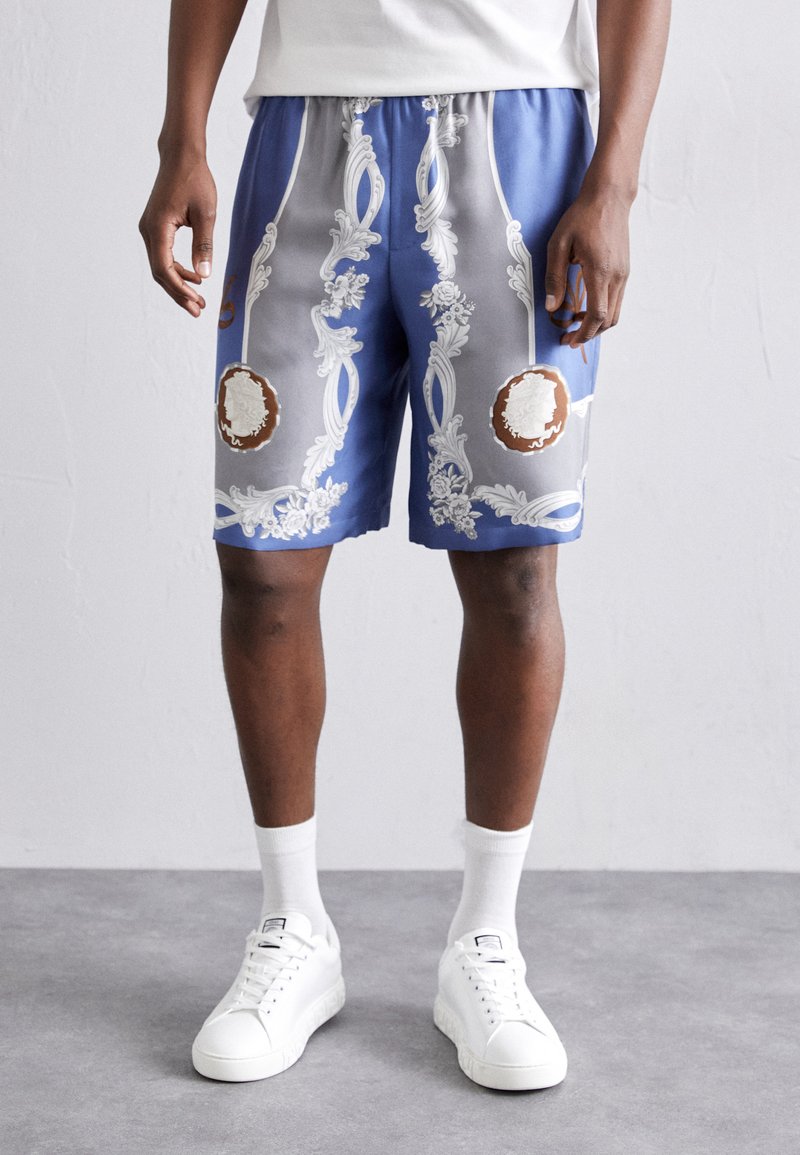 Blaue Shorts mit kunstvollen weißen Blumenmustern und braunen Akzenten. Elastischer Bund mit Kordelzug, glattes Gewebe, knielanges Design.