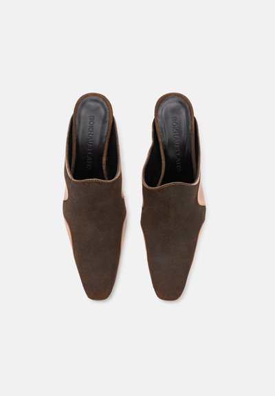 Mules en suède marron avec des bouts pointus et des talons ouverts, présentant un accent en cuir lisse sur les côtés et une marque embossée sur les semelles intérieures.
