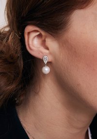 Kolczyki w kształcie kropli pereł mają design łezki, z posrebrzanym wkrętem ozdobionym małymi, przezroczystymi kamieniami oraz dużą białą perłą.