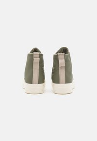 Sneaker high-top in pelle verde con una morbida fodera, accenti beige a contrasto, linguetta posteriore e suola in gomma bianca.