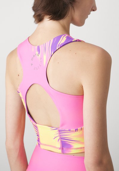 Fitted athletic crop top in bright pink, featuring a purple and yellow abstract pattern, back cutout, and smooth stretchy fabric.