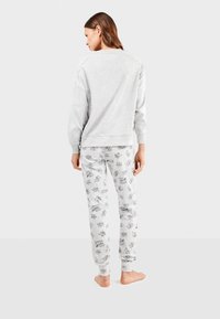 Sweatshirt gris à manches longues et ourlet côtelé, associé à un pantalon de pyjama gris clair orné d'impressions de personnages de dessin animé en noir.