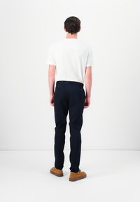 Pantalon marine à devant plat, avec cinq poches et passants de ceinture. Associé à un t-shirt blanc à manches courtes et des chaussures décontractées marron.