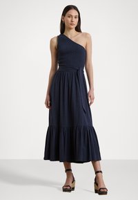 Asymmetriski yhden olkaimen mekko tummansinisena, jossa on kuminauhakoristelu bodice, vyötärösidonta ja kerrostettu helma. Yhdistetty mustiin korokepolkimiin.