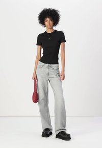 T-shirt nera aderente a maniche corte abbinata a jeans svasati grigi chiari. Il modello tiene una piccola borsa rossa e indossa scarpe con plateau nere e chunky.