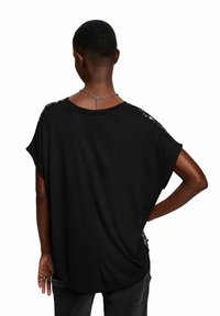 Camiseta negra de gran tamaño con mangas cortas, escote redondo y detalles decorativos en los hombros. Fabricada con una tela suave y un corte relajado.