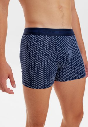 Marineblå boxershorts med et lille hvidt blomstermønster, der har en kontrastfarvet taljeelastik mærket "JBS UNDERWEAR." Blødt, strækbart stof.