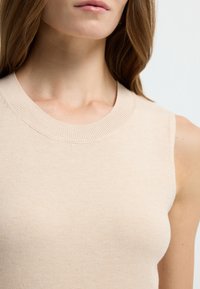 Beige mouwloze sweater met een ribbelstructuur ronde hals, met een zachte brei textuur en een aansluitende pasvorm. Geen zichtbare patronen of accenten.