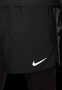 Calções atléticos pretos feitos de material leve com um bolso lateral. Apresentam um logótipo branco proeminente da Nike na bainha.