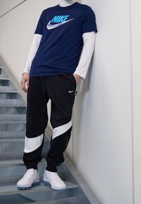 Marinblå Nike T-shirt med turkos logotyp, lager på lager över en vit långärmad skjorta. Svarta joggare med vita accenter och vita sneakers.