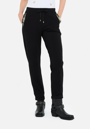 Pantaloni jogging neri con accenti di perline sulle tasche, cintura con laccio e caviglie elasticizzate, abbinati a stivaletti neri con cinturini borchiati.