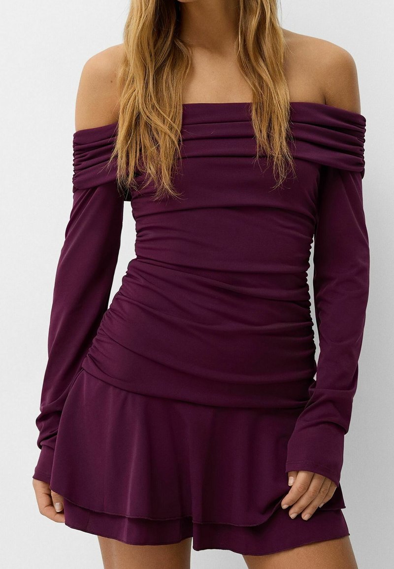 Lila off-shoulder klänning med långa ärmar, rynkad textur och lager på lager kjol, tillverkad av elastiskt material.