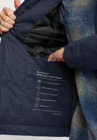 Marine buitenjack met Teflon EcoElite® stof, zwart gewatteerde voering en een binnenlabel met prestatie-specificaties.