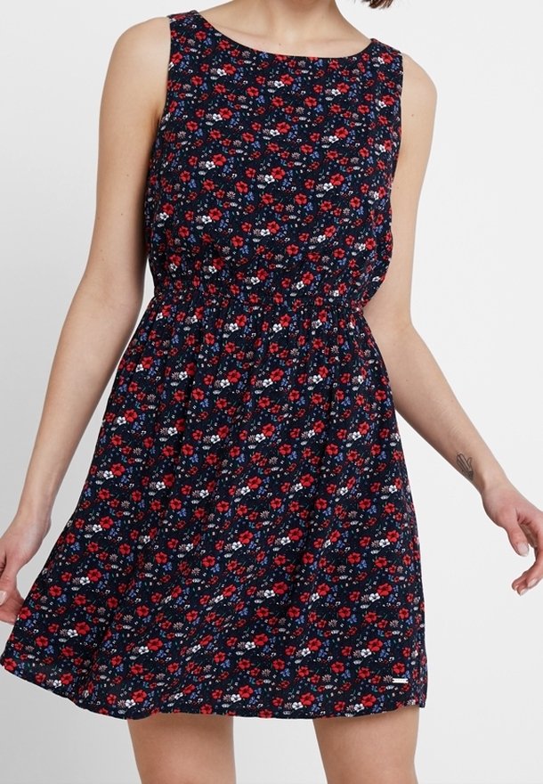 Robe sans manches bleu marine avec motif floral rouge, blanc et bleu, taille cintrée, portée par une personne debout visible des épaules jusqu'au milieu de la cuisse.