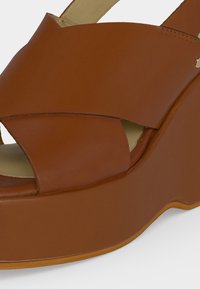 Καφέ δερμάτινο σανδάλι με πλατφόρμα, φαρδιές σταυρωτές λουρίδες και παχιά σόλα με ελαφρύ πέλμα ορατό.