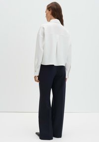 Blusa bianca strutturata con collo a camicia, maniche con polsini e piega posteriore, abbinata a pantaloni blu navy a gamba larga. Tessuto dalla superficie liscia.
