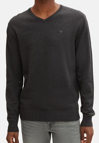 Donkergrijze v-hals sweater van gebreid stof, met lange mouwen en een geribde zoom. Subtiel logo detail op de borst.