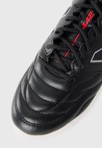 Chaussure de football noire avec cuir texturé, conception rembourrée, accents rouges et une étiquette "442" bien en vue sur le côté. Les lacets sont noirs.