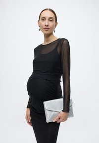 Fekete ruha hosszú, áttetsző ujjakkal, apró csillogó díszítésekkel. Ezüst kis táskával párosítva. Testhez simuló sziluett, kismamaruházatra tervezve.