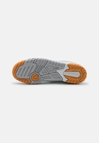 Gray athletic shoe outsole featuring a textured rubber surface, pronounced tread pattern, and an orange accent in the heel area.