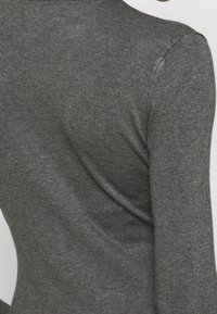 Maglione grigio scuro a coste con collo alto e design aderente. Texture liscia con una leggera lucentezza e senza cuciture o decorazioni visibili.