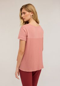 Růžové tričko s krátkými ohrnutými rukávy a skládáním na zádech, s hladkým předním dílem a strukturovanými, splývavými sklady vzadu.