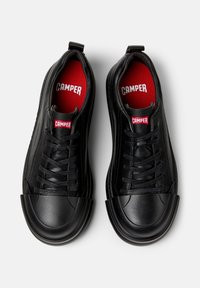Svarta sneakers med rund tå och gummikåpa, med röda innersulor och "CAMPER"-logotyp på tungan och innersulan.