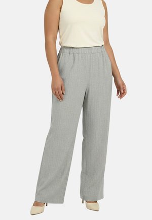 Femme portant un pantalon large gris clair avec une taille élastique et un haut crème sans manches, associé à des talons pointus crème.