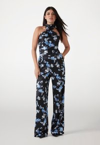 Salopetă florală neagră cu guler halter și detaliu legat, realizată dintr-o țesătură satinată netedă cu modele de flori albastre și albe. Design cu picioare largi.