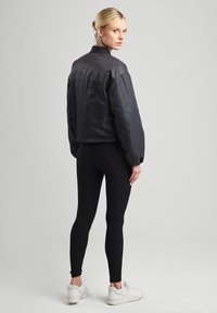 Black bomber jacket with a relaxed fit, ribbed collar, and smooth fabric. Paired with fitted black leggings and white sneakers.