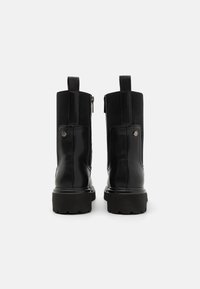 Botas de tobillo de cuero negro con paneles elásticos acanalados, cierre de cremallera y suela gruesa. Incluyen un acento decorativo de metal en el costado.