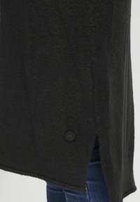 Černý pletený svetr s jemnou texturou, s bočním rozparkem a černým knoflíkem na lemu. Hladký povrch, ležérní design.