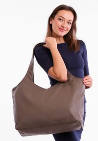 Brown leather tote bag with a soft, smooth texture, large size, and U-shaped handle. Features minimalistic design and subtle branding.