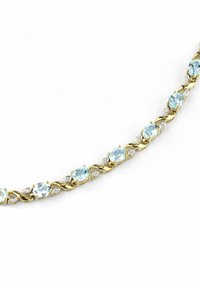 Zelta ķēde, kurā mijas gaiši zili akmeņi un caurspīdīgas akcenti, ar sakrustotu dizainu, kas piešķir papildu tekstūru un detaļas.