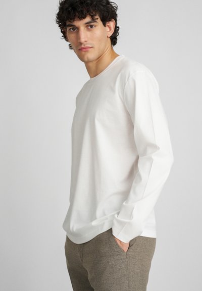 Chemise blanche à manches longues en coton doux, avec un col rond et une coupe décontractée. Associée à un pantalon léger marron texturé, avec des poches.