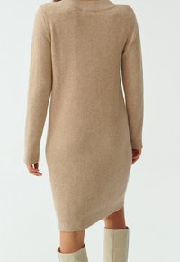 Robe en maille beige à manches longues, avec poignets et ourlet côtelés. Texture douce, coupe ajustée s’effilant vers le bas.