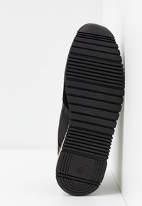 Czarna podeszwa sneakerów z teksturowanym gumowym wzorem, z głębokimi rowkami zapewniającymi przyczepność i schludnym designem. Rozmiar oznaczony jako 37.