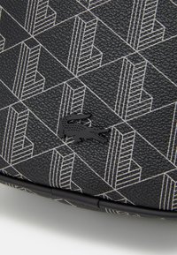 Black textured material with a geometric white pattern and a black crocodile logo. Round shape with a reinforced edge detail.