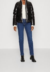 Sort, blank, pufferjakke med høj krave og lynlås, båret over en cremefarvet top og blå jeans, suppleret med sorte ankelstøvler.